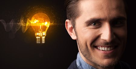 Portrait of a young businessman with a lightbulb next to him on a dark background