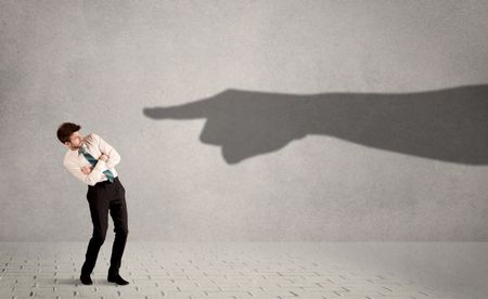 Business person looking at huge shadow hand pointing at him concept on background
