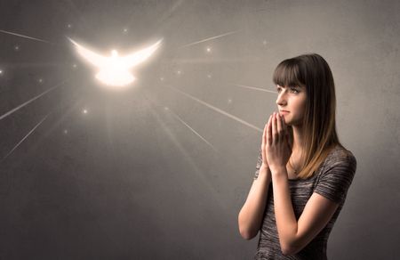 Young woman praying on a grey background with a sparkling bird above her