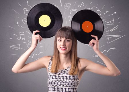 Young lady holding vinyl record on a grey background with mixed scribbles behind her