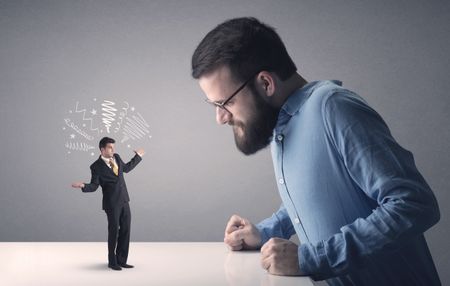 Young professional businessman being angry with an other miniature businessman who has scribbles above his head