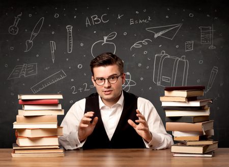 A passionate young teacher sitting at school desk with pile of books in front of blackboard drawn full of back to school items concept.