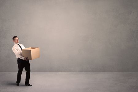 A well dressed young office worker holding an empty paper box with clear concrete wall background concept.