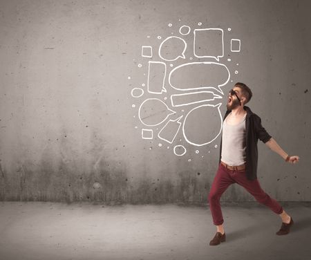 A comic hipster guy shouting in front of grey urban concrete wall with drawn empty text bubbles around his mouth concept