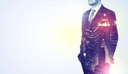 Young businessman thinking and standing with night skyscraper background