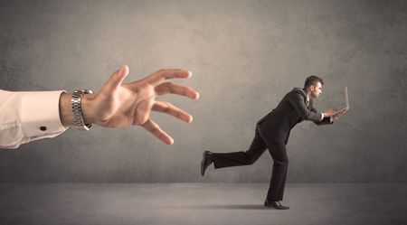 Young miniature businessman running from a big hand with grey background