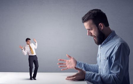 Young professional businessman being angry with an other miniature businessman in front of a grey background