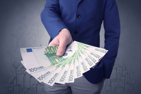 Young businessman holding large amount of bills with grungy drawings of a city and numbers behind him