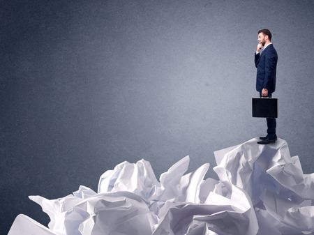 Thoughtful young businessman standing on a pile of crumpled paper 