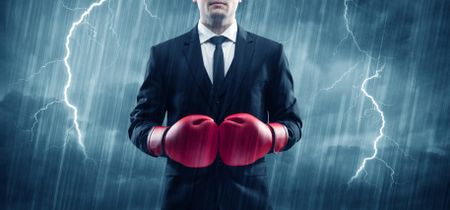 A dangerous sales person getting ready for a fight concept with red boxing gloves and thunder lightning in background.