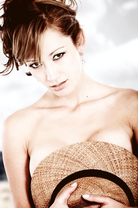 fashion girl at the beach covering her breasts with a straw hat - high key