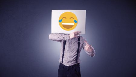 Young businessman hiding behind a laughing emoticon on cardboard