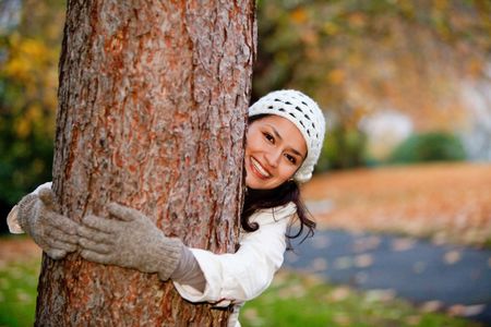 Autumn woman hugging a tree and smiling outdoors