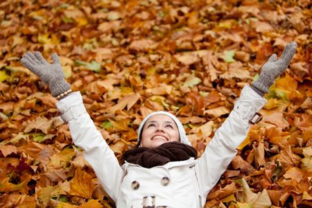 Happy autumn woman lying over leaves and smiling