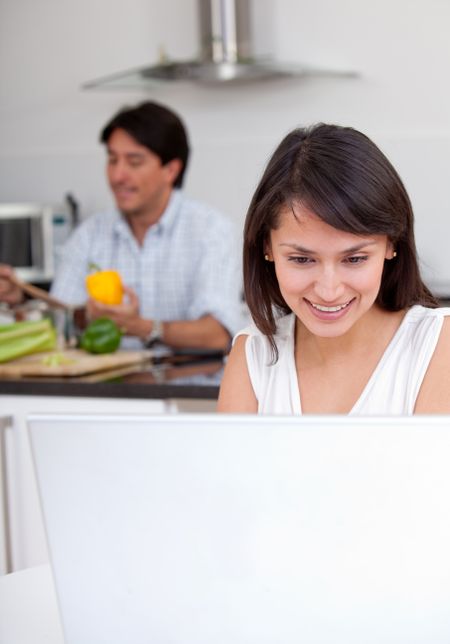 Busy woman working at home on a laptop while partner is cooking