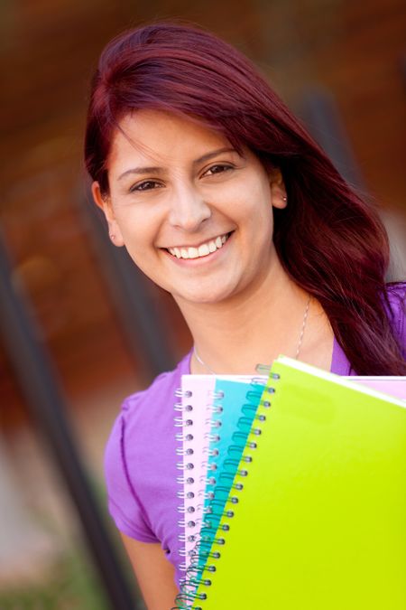 Female student carrying notebooks outdoors and smiling