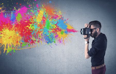 A retro hipster male taking photograph with a vintage camera of an urban wall with paint splatter concept