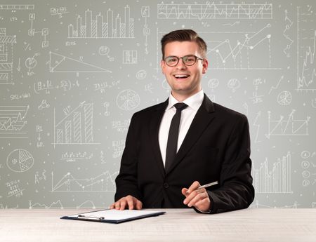 Young handsome businessman sitting at a desk with white graphs and calculations behind him