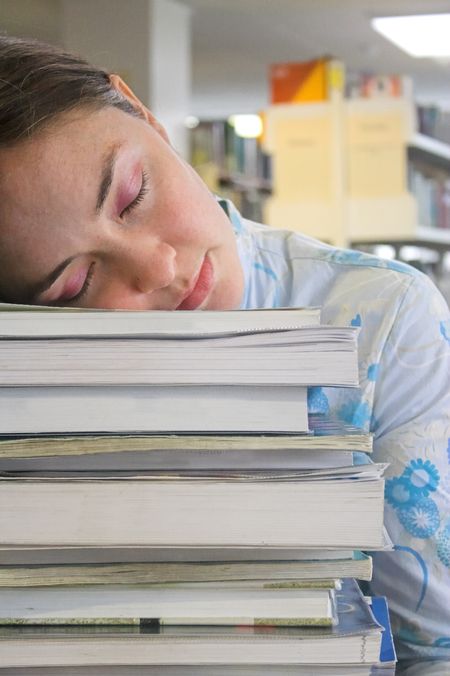 Beautiful student sleeping in the library on top of some books.