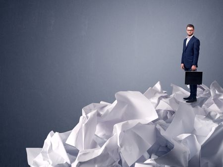 Thoughtful young businessman standing on a pile of crumpled paper with a light grey background