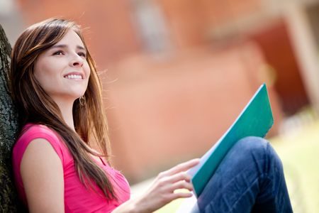 Thoughtful female student sitting outdoors and smiling