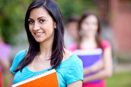 Female student carrying notebooks outdoors and smiling