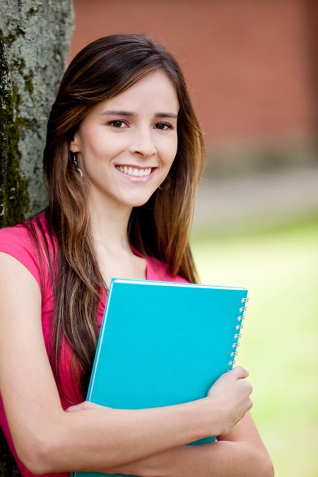 Happy female student carrying notebooks outdoors