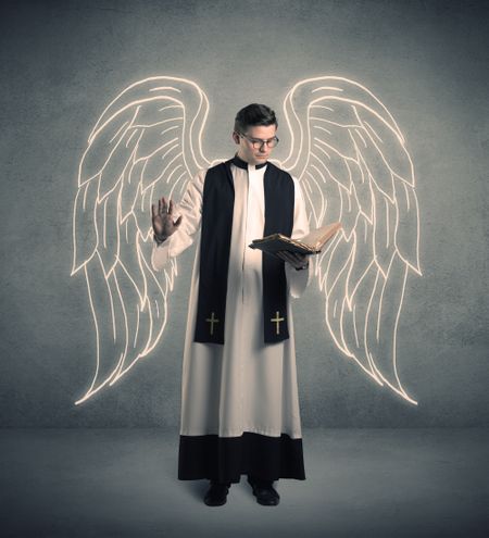 A young male priest with drawn large angel wings standing with the holy bible in his hands concept.