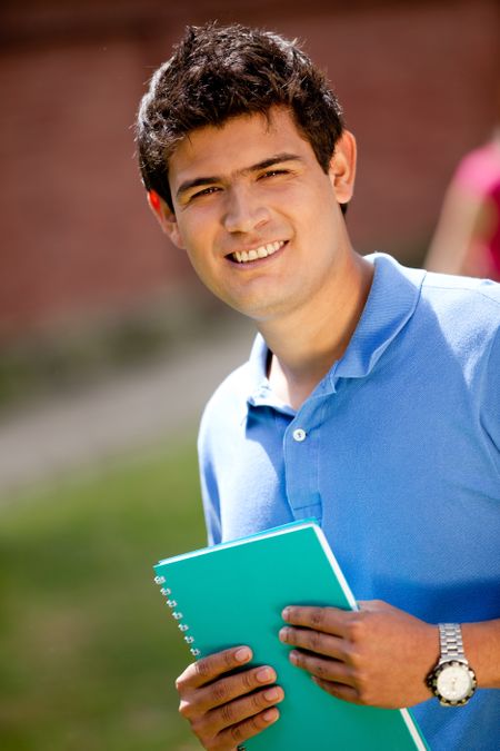 Male student carrying notebooks outdoors and smiling