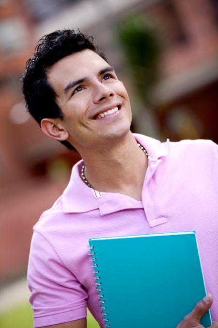 Male student with a notebook outdoors and smiling