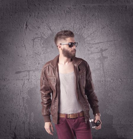 A hipster fashion model guy in casual clothing stnading with mobile phone in front of concrete urban wall background concept