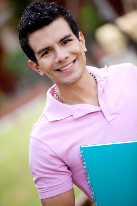 Male student with a notebook outdoors and smiling