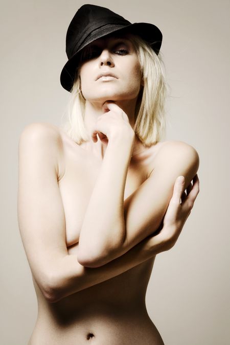 Young female model wearing a black hat over one eye.  Her upper body is covered by both arms.