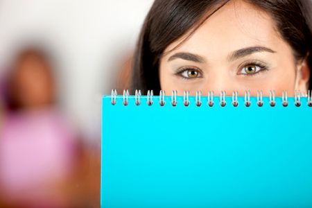 Beautiful female student covering her face with a notebook