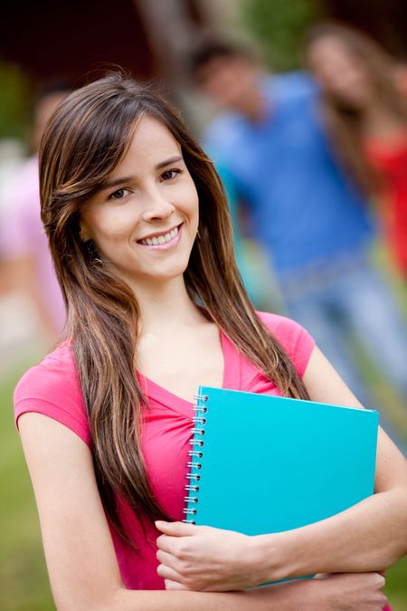 Female student carrying notebooks outdoors and smiling