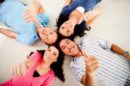 Group of friends with their heads together on the floor and thumbs up - isolated