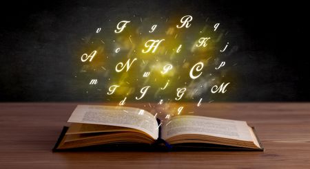 Glowing yellow alphabet letters coming out of an open book 