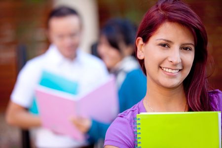 Female student carrying notebooks outdoors and smiling