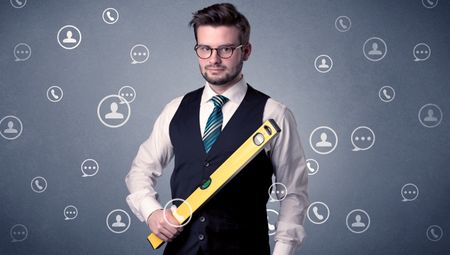 Thoughtful businesman holding tool with communication symbols around