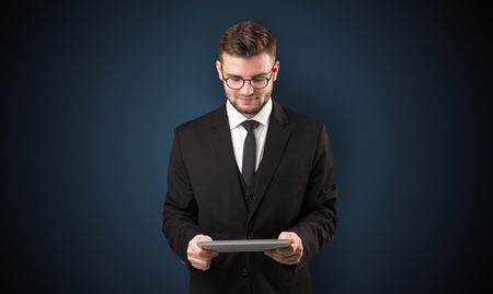 Handsome spectacled businessman holding a tablet with dark background
