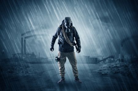 Gas masked survival man coming with arms on his hand  in a demolished dark environment 