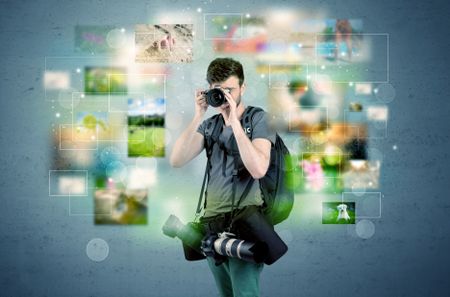 A young amateur photographer with professional camera equipment taking picture in front of blue wall full of faded pictures and glowing lights concept