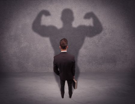 A young salesman standing with his back, looking at his musculous shadow reflecting on the wall concept