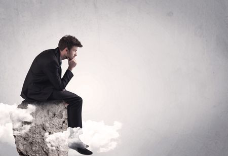 An elegant  smart businessman with laptop sitting in empty grey space on top of a cliff, between clouds concept