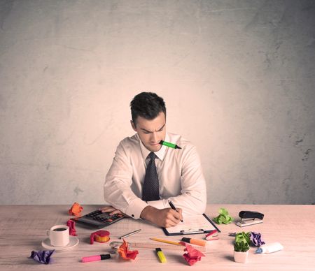 A young office worker sitting at desk working with keyboard, papers, highliter in front of empty clear background wall concept