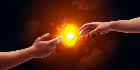 Two naked male hands about to touch, lighting a bright flame with smoke in red sky background concept