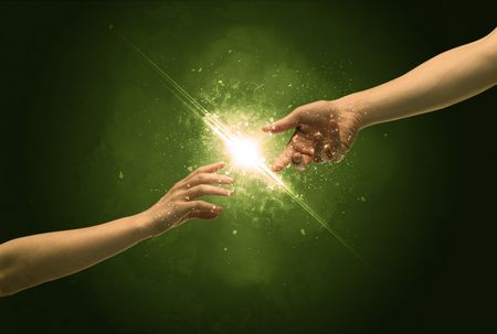 Two naked male hands about to touch, lighting the spark with modest explosion in front of green background concept