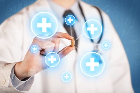 A male doctor in coat in front of a blue wall holding a pill between his fingers with lines and white crosses in circles