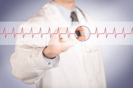 A male doctor in white coat with a stethoscope on one shoulder holding a pill between his fingers focused on a heartbeat graph