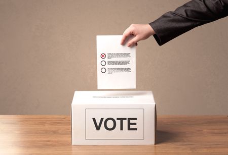 Close up of male hand putting vote into a ballot box, on grungy background